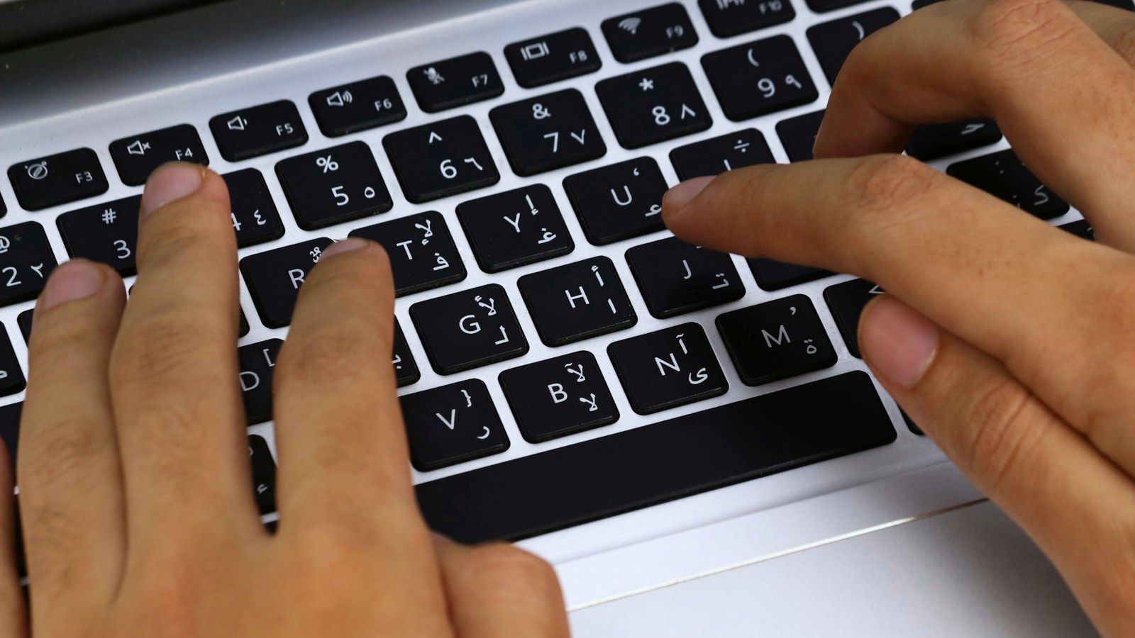 Hands typing on a bilingual Arabic and English laptop keyboard, the input an Arabic storefront search must handle