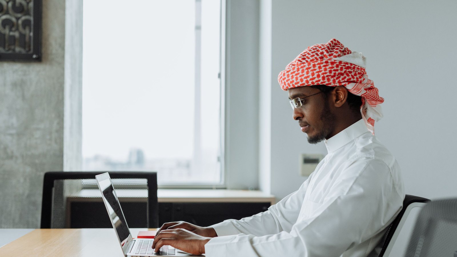 Finance specialist in a ghutra working on a laptop at a Gulf office desk, checking e-invoice results
