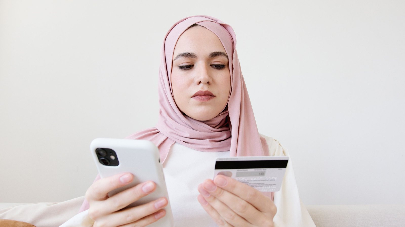 Woman in a hijab paying for an online order on her phone with a credit card at home