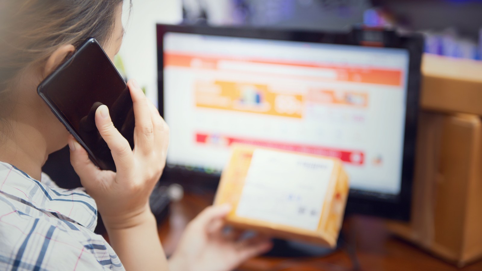 Shopper on the phone holding a delivered parcel in front of an online store, chasing an order query or a return