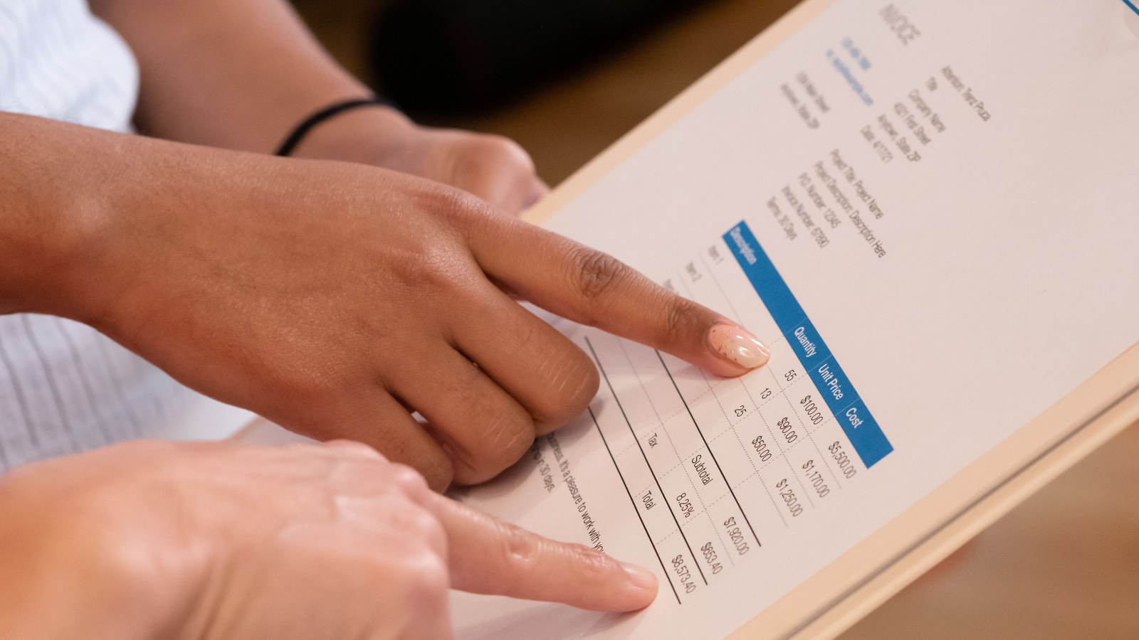 Two people pointing at an invoice's quantity, unit price, tax and total lines, the detail a tax invoice must carry