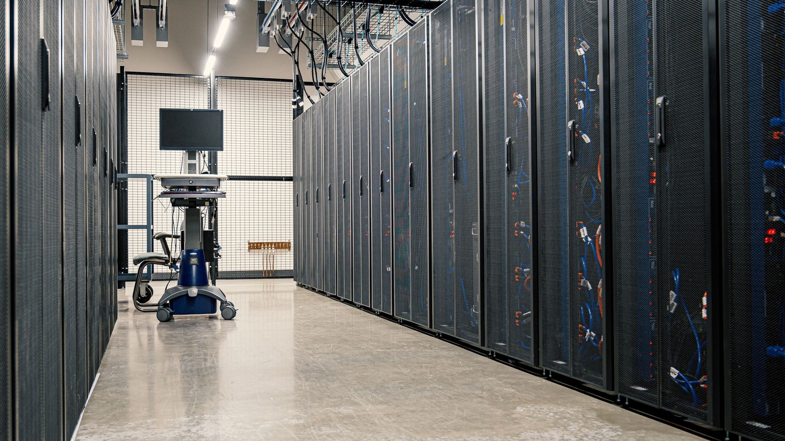 Data-center aisle lined with server racks and a mobile ops workstation, showing the concrete infrastructure behind hidden hosting and DevOps costs.