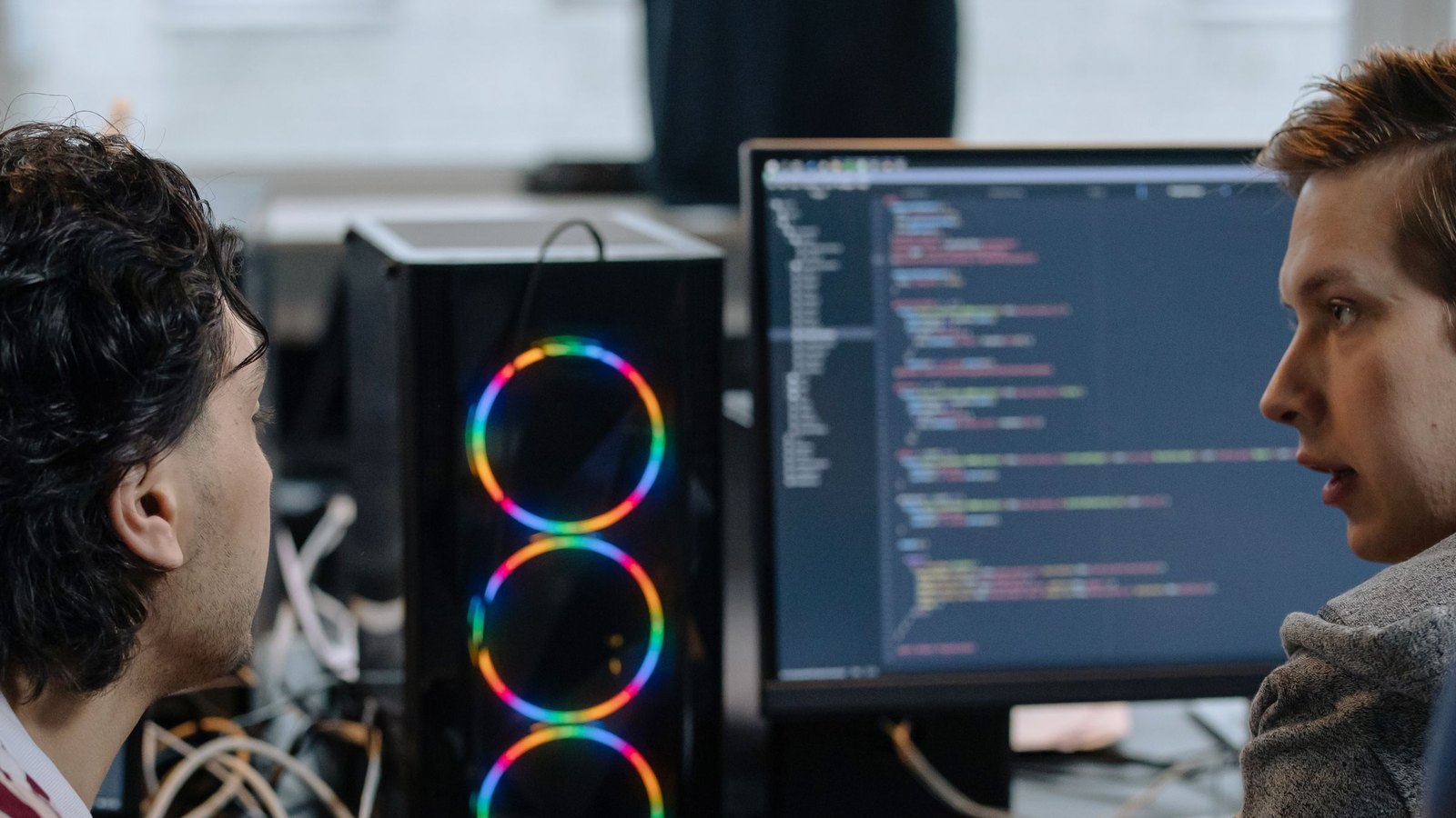 Two developers reviewing integration code together on a monitor next to a workstation
