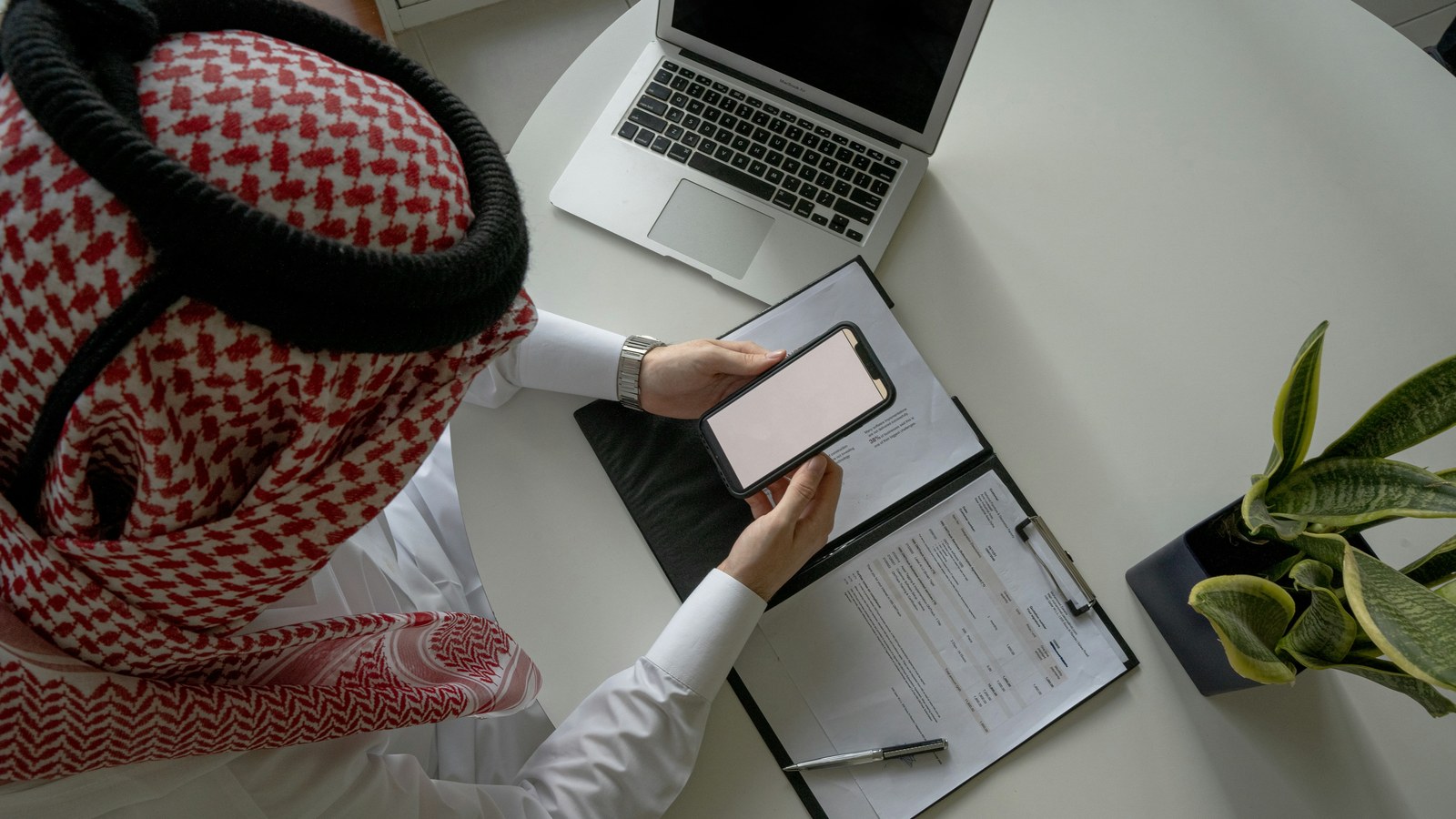 Gulf finance reviewer checks a settlement statement against a phone and laptop, matching UAE payouts to orders