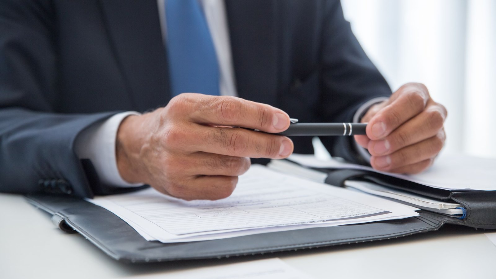 Buyer in a suit with pen in hand reviewing a supplier quote in a document folder before signing