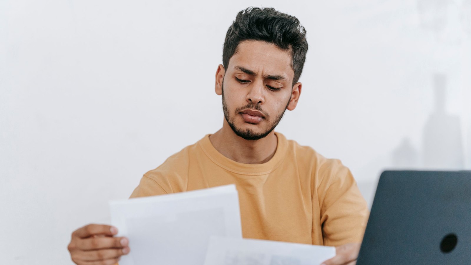 Man comparing two printed quote documents beside his laptop, frowning at a mismatch