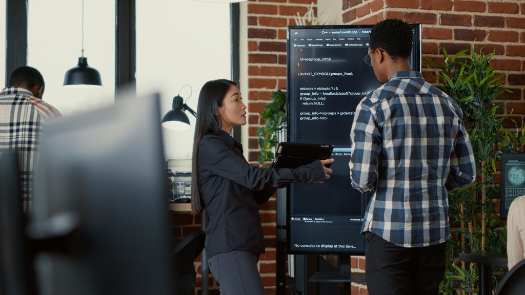 Team of coders analyzing code on wall screen tv comparing errors using digital tablet