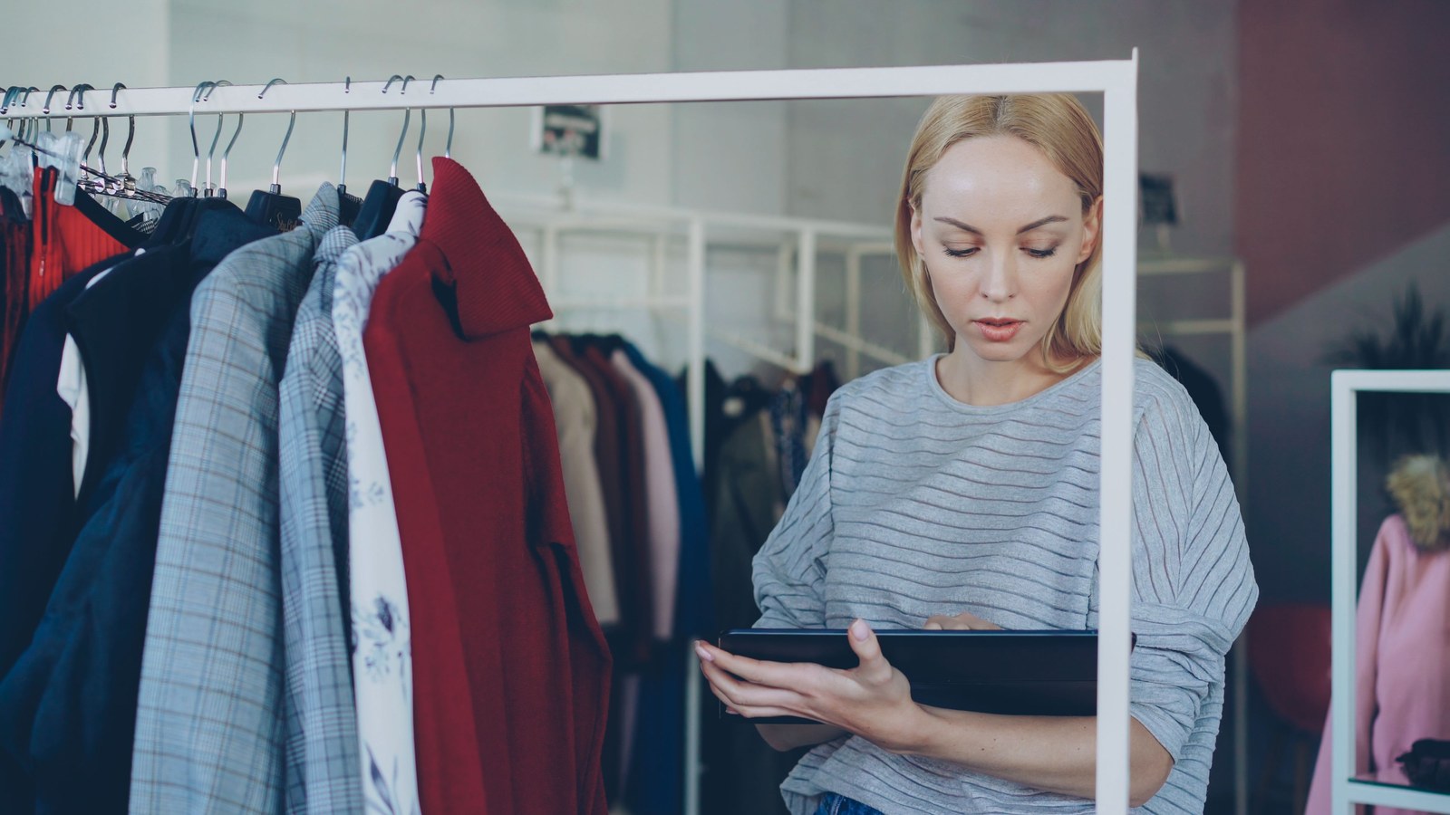 Buyer checking an account catalogue on a tablet beside sample garment rails, as in account-based B2B ordering
