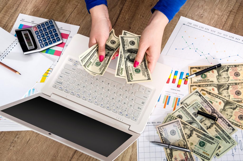 money in the hands of a laptop and graphics