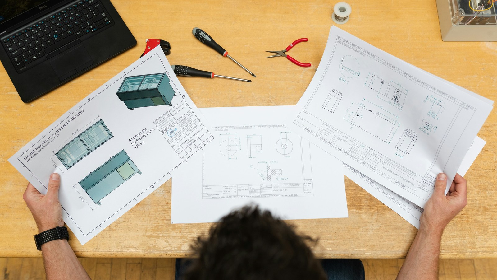 Engineer reviewing printed technical drawings and specs at a desk before pricing a custom order